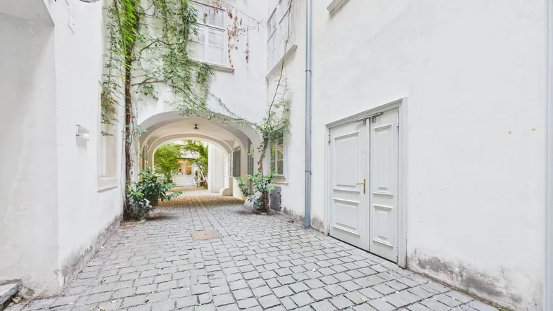 Historischer Innenhof mit Kopfsteinpflaster und begrünten Wänden, der zu weiteren Gebäudeteilen führt.