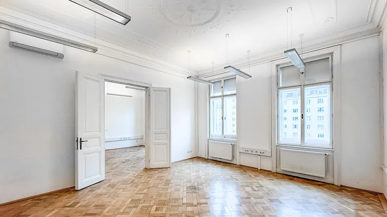 Geräumiges Zimmer mit Fischgrätparkett, hohen Decken und Stuckverzierungen, ideal für Wohn- oder Büronutzung.