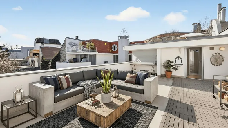 Sonnige Dachterrasse mit moderner Lounge-Möblierung und weitem Blick über die Dächer der Stadt.