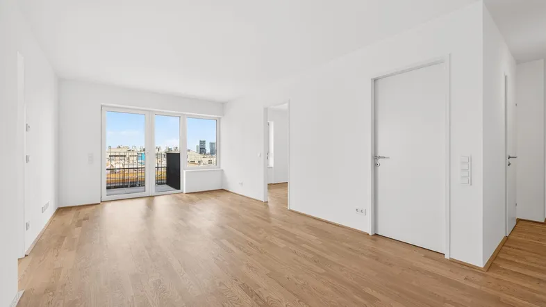 Helles, leeres Wohnzimmer mit Parkettboden und Zugang zu einem kleinen Balkon mit Stadtblick.
