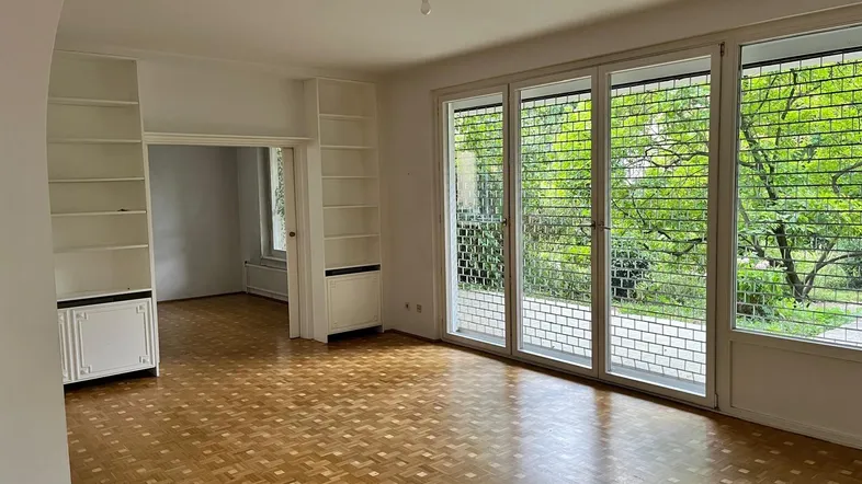 Helles Wohnzimmer mit Parkettboden, großen Fenstern und Blick ins Grüne.