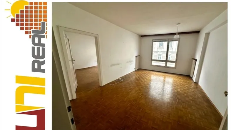 Helles, leeres Wohnzimmer mit Fischgrätparkettboden und Blick auf die gegenüberliegenden Gebäude.