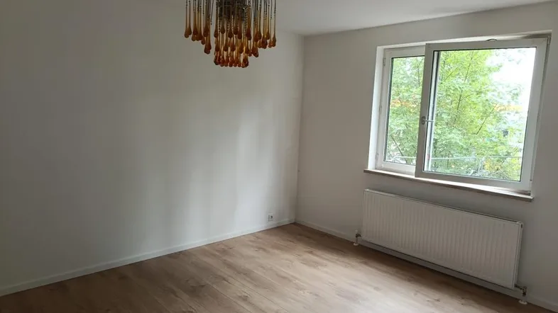 Heller Raum mit Laminatboden, großem Fenster und einer dekorativen Deckenleuchte.