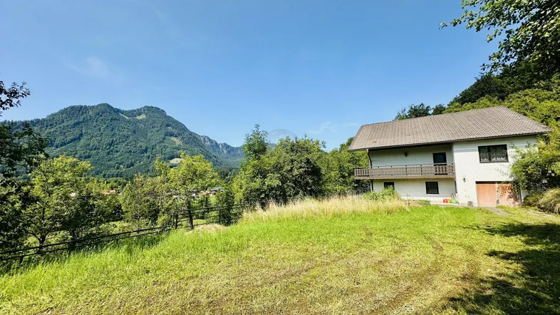 Älteres Haus mit großem, ungemähtem Rasen und weitem Blick auf die umliegende Berglandschaft.