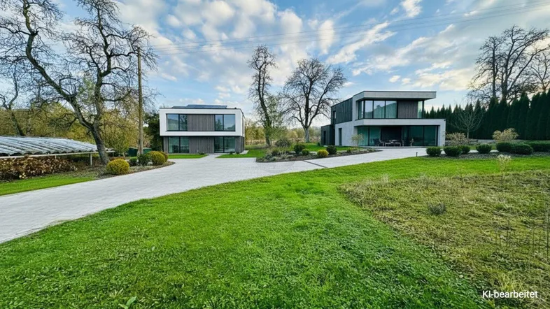 Zwei moderne Häuser mit klaren Linien, umgeben von einer weitläufigen Grünfläche und einer gepflasterten Zufahrt.