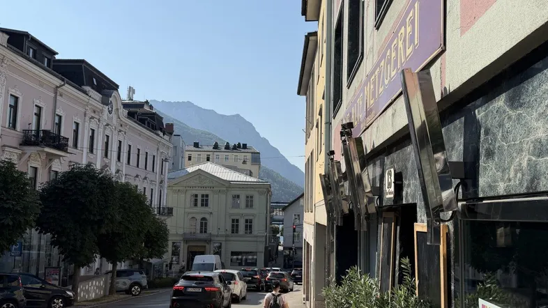 Blick auf eine belebte Straße mit historischen Gebäuden und Bergen im Hintergrund unter klarem Himmel.