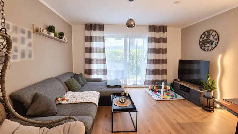 Helles Wohnzimmer mit großem Sofa, Holzboden und Zugang zum Balkon, ideal für Familien.