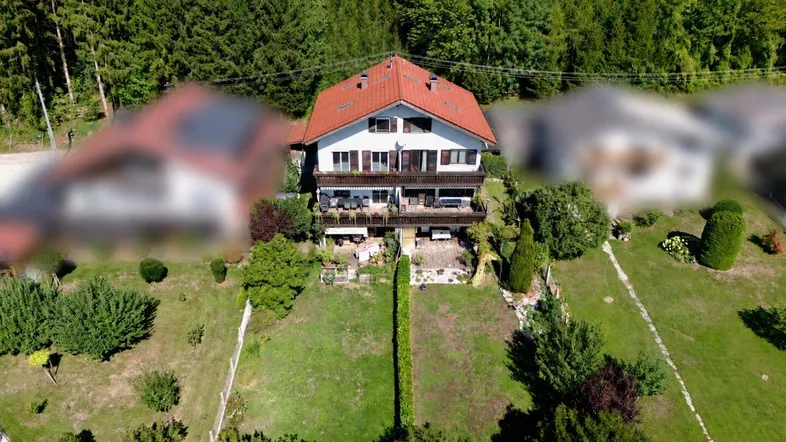 Luftaufnahme eines Hauses mit rotem Ziegeldach, Balkonen und großem Garten, umgeben von Wald.