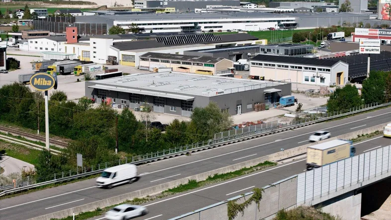Luftaufnahme eines Gewerbegebiets mit mehreren Hallen und einer Autobahn im Vordergrund.