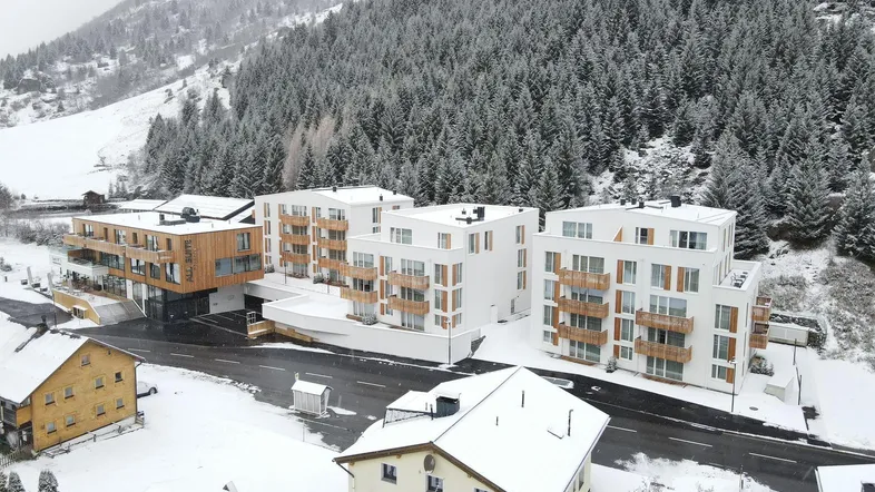 Moderne Wohngebäude in einer verschneiten Berglandschaft, umgeben von dichtem Wald.