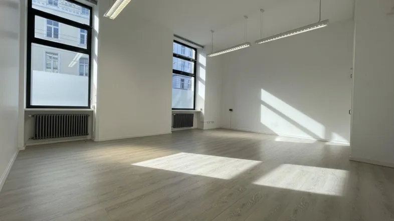 Heller, leerer Büroraum mit großen Fenstern, hellem Laminatboden und viel natürlichem Licht.