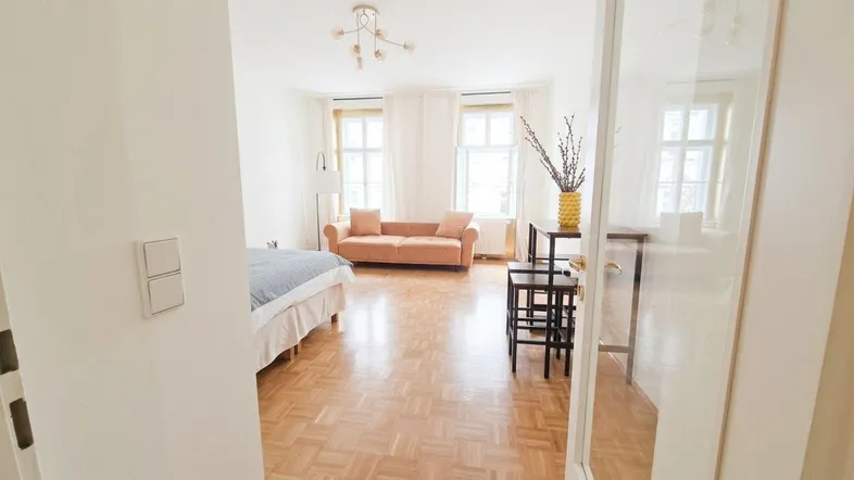 Helles Wohnzimmer mit Parkettboden, beigem Sofa und zwei großen Fenstern.