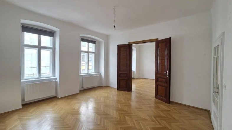 Geräumiges, helles Wohnzimmer mit Fischgrätparkett und hohen Decken in einem Altbau.