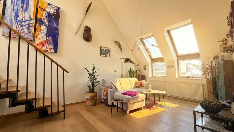 Helles Wohnzimmer mit Holzboden, Dachschrägen und offener Treppe, durchflutet von Sonnenlicht.