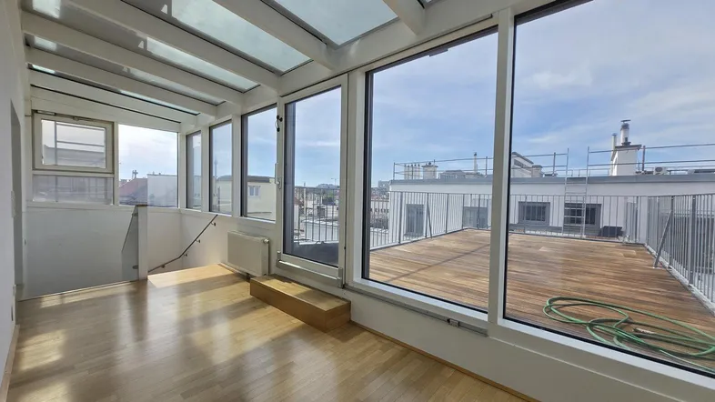Heller Wintergarten mit Holzboden und großen Glasflächen, der zu einer Dachterrasse führt.