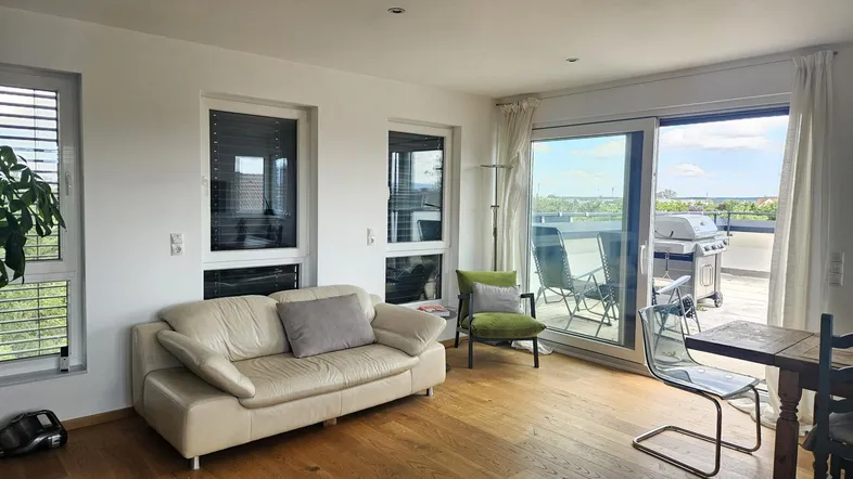 Helles Wohnzimmer mit beigem Sofa, Holzboden und Zugang zu einer großen Terrasse mit Grill.