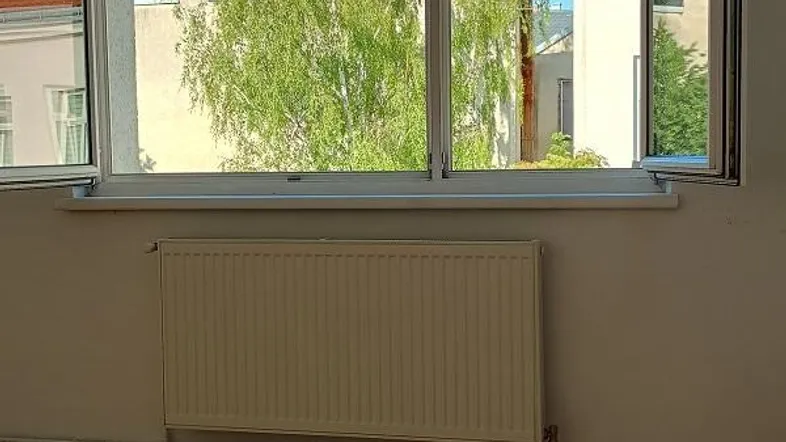 Heller Raum mit Holzboden und Blick auf Bäume und umliegende Gebäude.