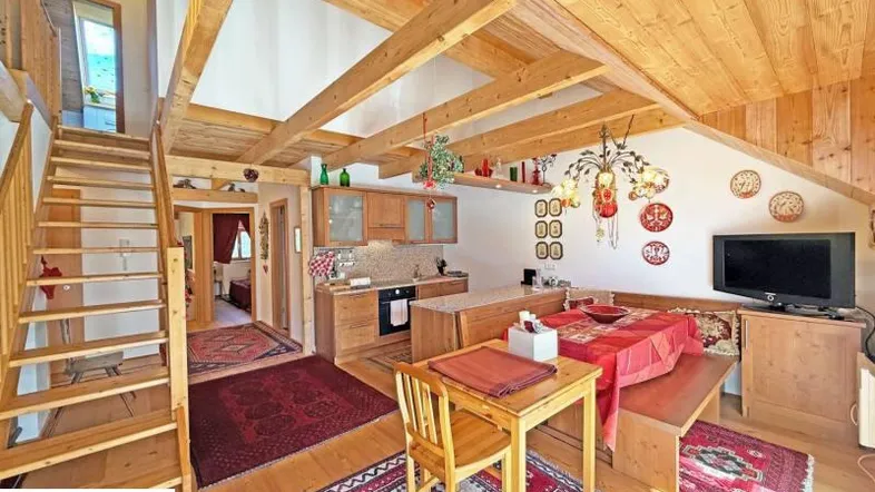 Gemütlicher offener Wohn- und Essbereich mit Holzbalkendecke, integrierter Küche und Treppenzugang.