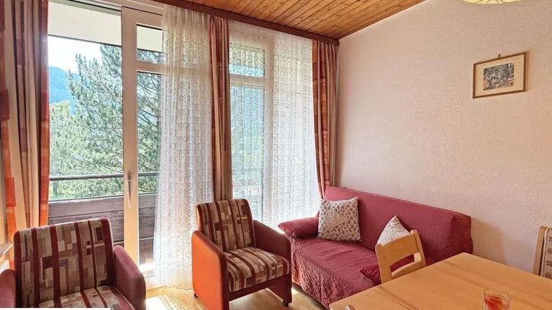 Gemütliches Wohnzimmer mit Holzbalkendecke, Sitzgelegenheiten und Zugang zum Balkon.
