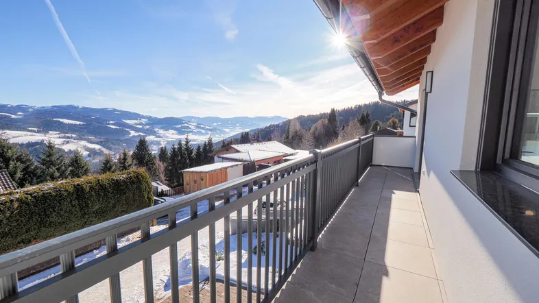 Sonniger Balkon mit atemberaubendem Blick auf die verschneite Berglandschaft und blauen Himmel.
