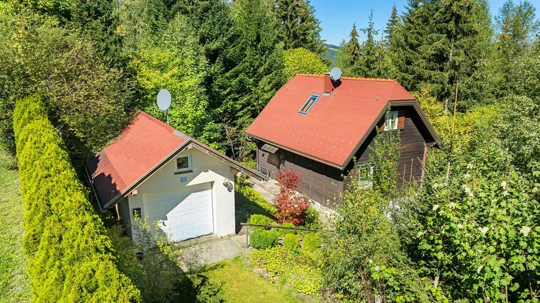 Luftaufnahme zweier Gebäude mit roten Dächern, umgeben von dichtem Wald und grüner Natur.