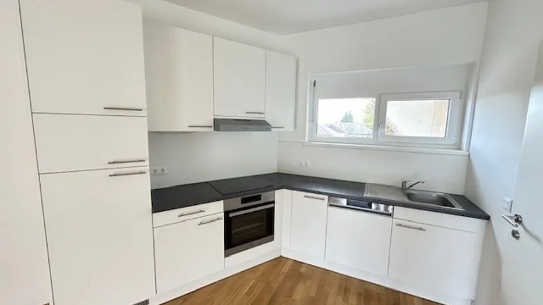 Moderne Einbauküche mit weißen Schränken, dunkler Arbeitsplatte und Fenster für natürliches Licht.