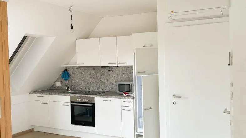 Helle Einbauküche in Dachgeschosswohnung mit weißen Schränken, Holzfußboden und Dachschräge.
