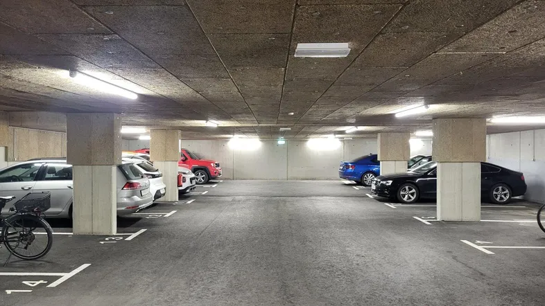 Geräumige Tiefgarage mit markierten Stellplätzen und abgestellten Fahrzeugen sowie Fahrrädern.