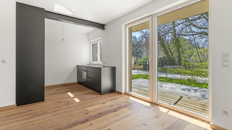 Helles Zimmer mit Holzboden, moderner Küchenzeile und Zugang zu einer Terrasse mit Gartenblick.