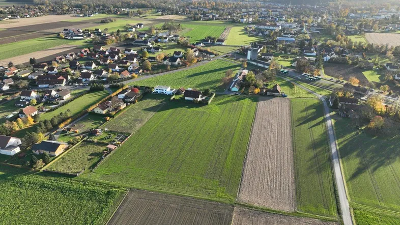 Luftaufnahme einer ländlichen Siedlung mit Feldern, Häusern und Straßen unter blauem Himmel.