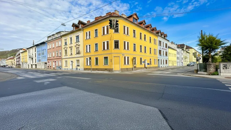 Buntes Eckgebäude an einer Kreuzung mit mehreren Stockwerken unter blauem Himmel.