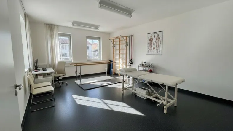 Heller Therapieraum mit moderner Ausstattung, dunklem Vinylboden und viel Tageslicht durch die Fenster.