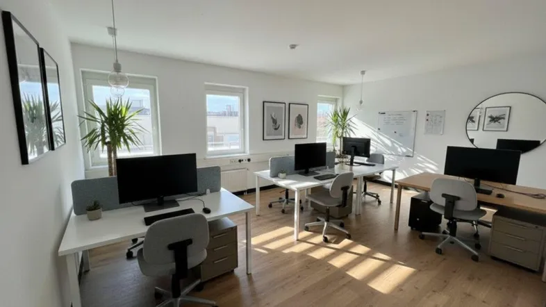 Helles und modernes Büro mit mehreren Arbeitsplätzen, Holzboden und großen Fenstern, die viel Tageslicht hereinlassen.