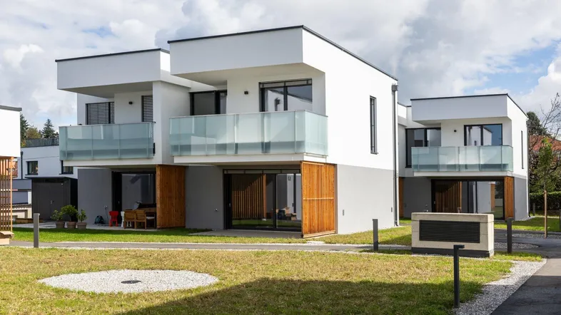Moderne Reihenhäuser mit weißer Fassade, grauen Akzenten und Balkonen in einer grünen Umgebung.