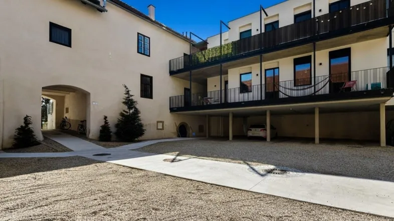 Außenansicht eines Gebäudekomplexes mit modernem Anbau, Balkonen und einem Kieshof.