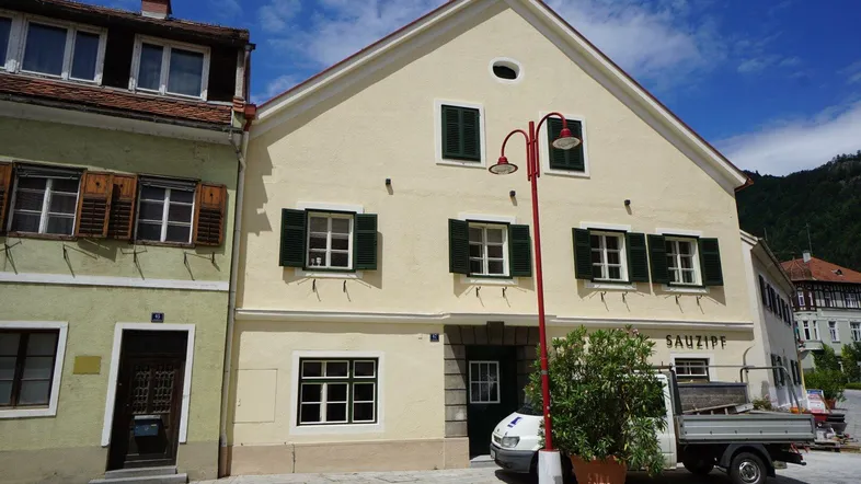 Traditionelles Gebäude mit gelber Fassade, grünen Fensterläden und einem roten Laternenpfahl davor.
