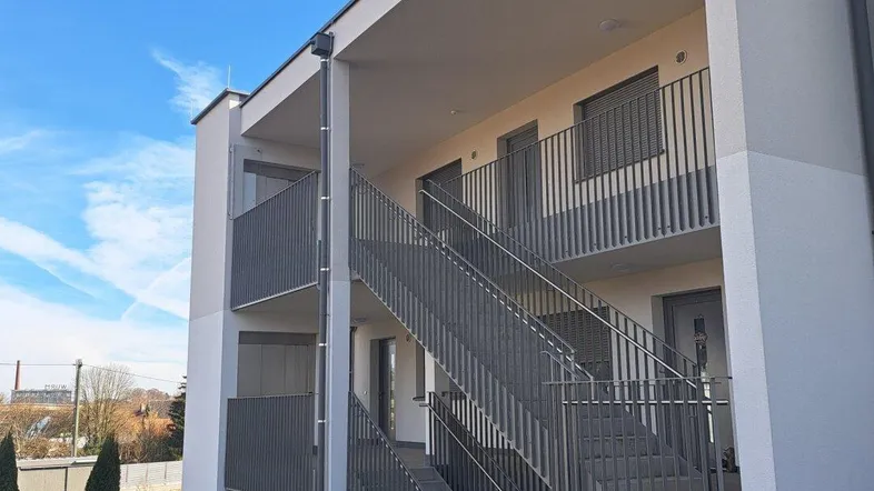 Moderne Wohnanlage mit Außentreppen und Balkonen unter blauem Himmel.