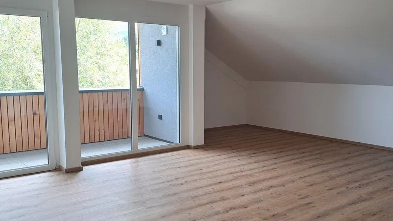 Geräumiger, heller Wohnbereich mit Laminatboden, Dachschräge und Zugang zu einem Balkon.