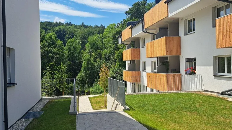Modernes Gebäude mit Holzverkleidung an den Balkonen und gepflegter Grünfläche unter blauem Himmel.