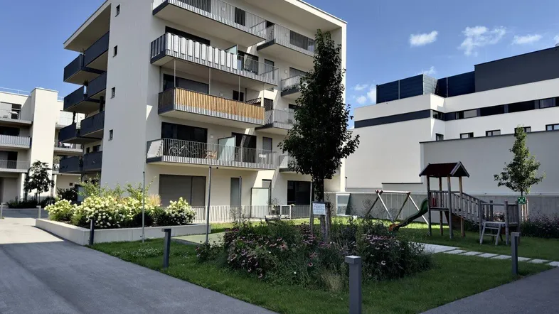 Modernes Wohngebäude mit weißer Fassade, Balkonen und einem Spielplatz im begrünten Außenbereich.