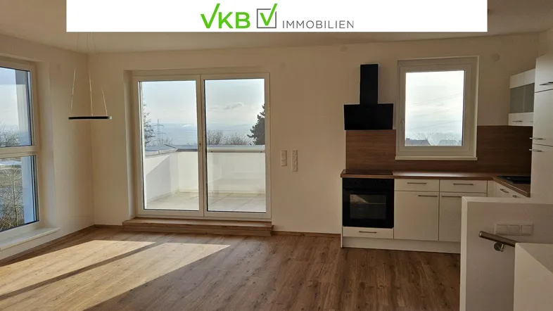 Heller Wohn- und Essbereich mit Holzboden, integrierter Küche und Zugang zum Balkon mit Weitblick.