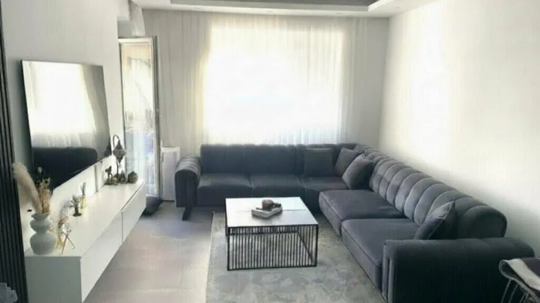 Gemütliches Wohnzimmer mit großem Ecksofa, Couchtisch und hellen Vorhängen.