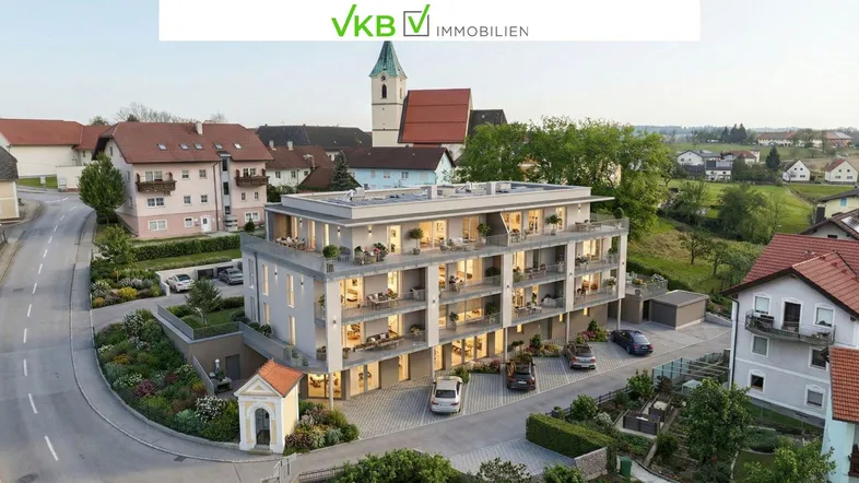 Eine moderne Wohnanlage mit mehreren Balkonen und Terrassen, eingebettet in eine ländliche Umgebung mit Kirche im Hintergrund.