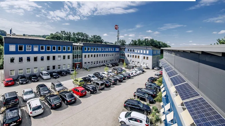Luftaufnahme eines modernen Bürogebäudes mit großem Parkplatz und Photovoltaikanlage auf dem Dach.