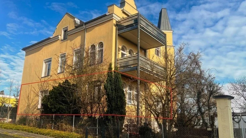 Historisches Gebäude mit gelber Fassade, Balkonen und einem markanten Turm, umgeben von kahlen Bäumen.
