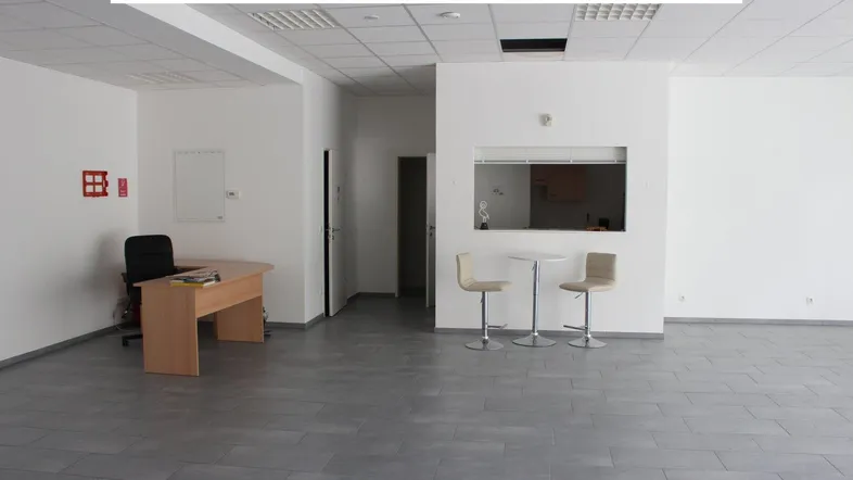 Geräumiger, heller Büroraum mit grauem Fliesenboden, einer kleinen Theke und einem Arbeitsplatz.