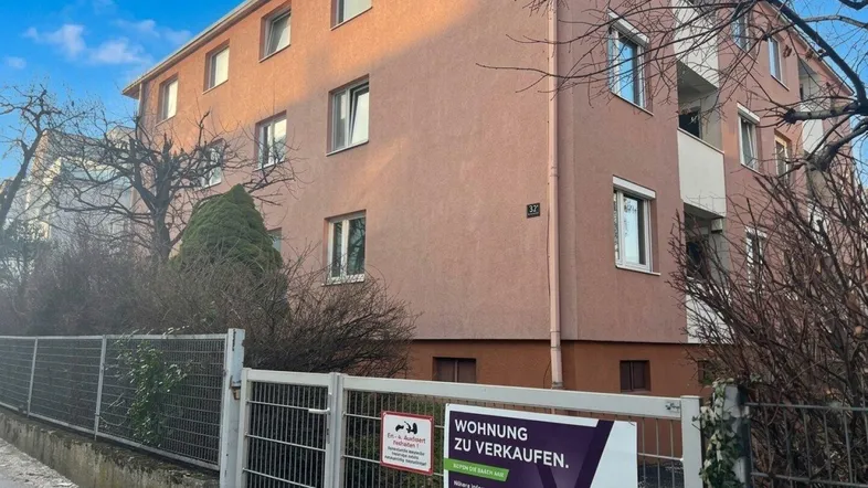 Mehrfamilienhaus mit mehreren Balkonen und Rollläden an den Fenstern, umgeben von Bäumen.