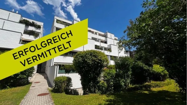 Weißes Mehrfamilienhaus mit gepflegter Grünanlage und sonnigem Eingangsbereich.