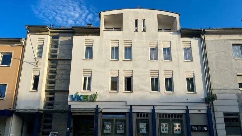 Mehrstöckiges Gebäude mit weißer Fassade und Geschäftsräumen im Erdgeschoss an einer Straße.