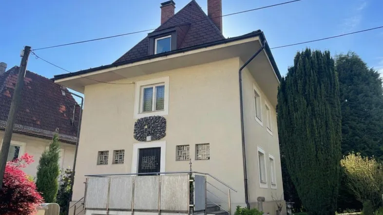 Gut erhaltenes Einfamilienhaus mit beiger Fassade, Mansarddach und kleinem Balkon am Eingang.